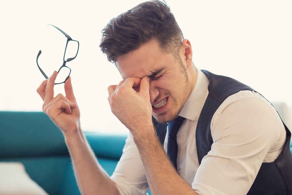 A man holding his glasses and rubbing his eyes in discomfort